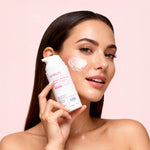 Woman applying cream to her face with a pink background