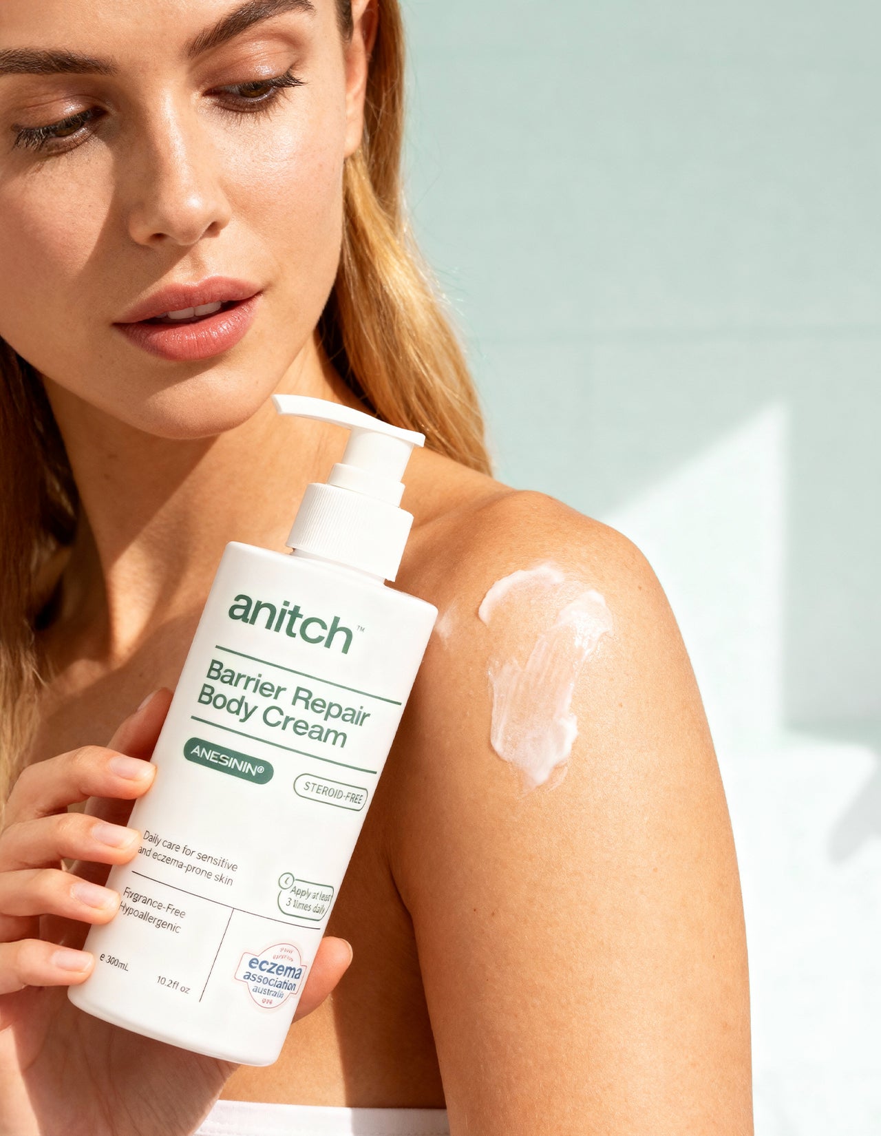 Woman applying anitch Barrier Repair Body Cream to her shoulder with a light background