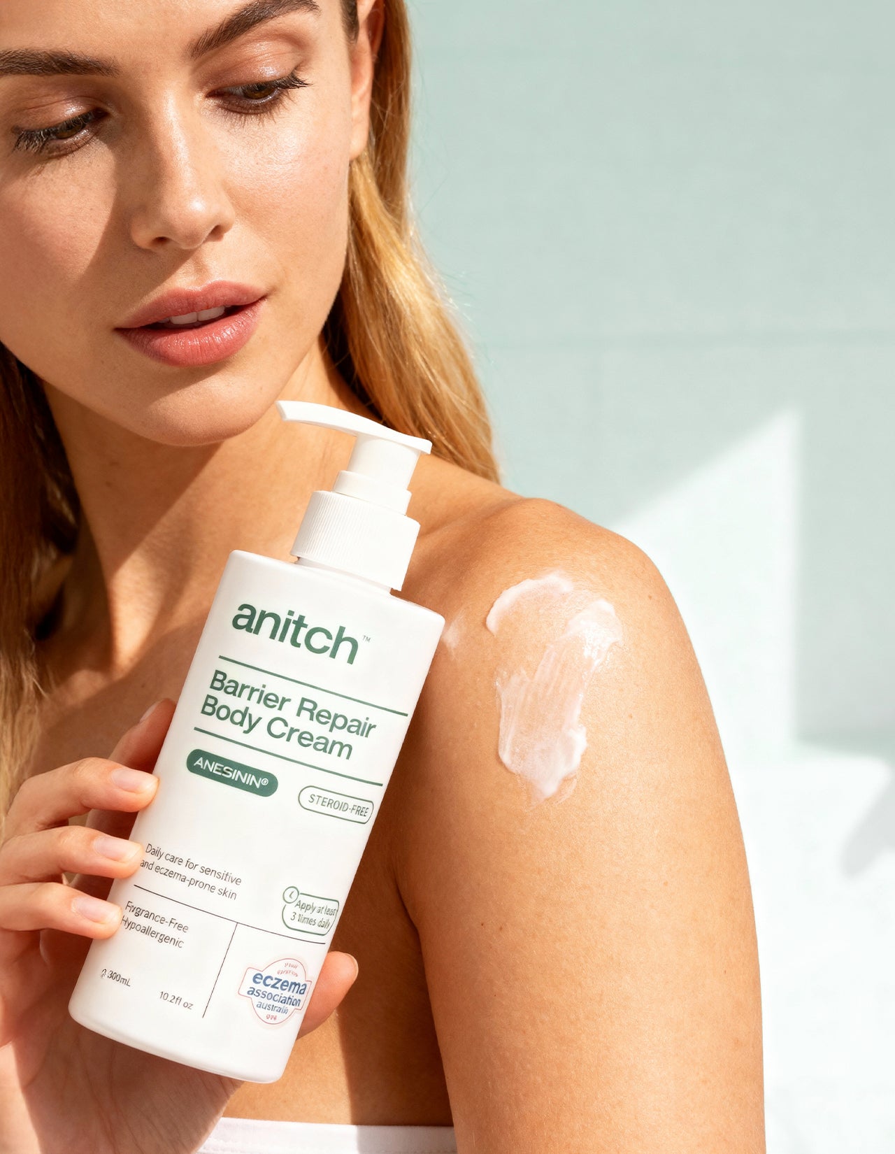 Woman applying anitch Barrier Repair Body Cream to her shoulder against a light background